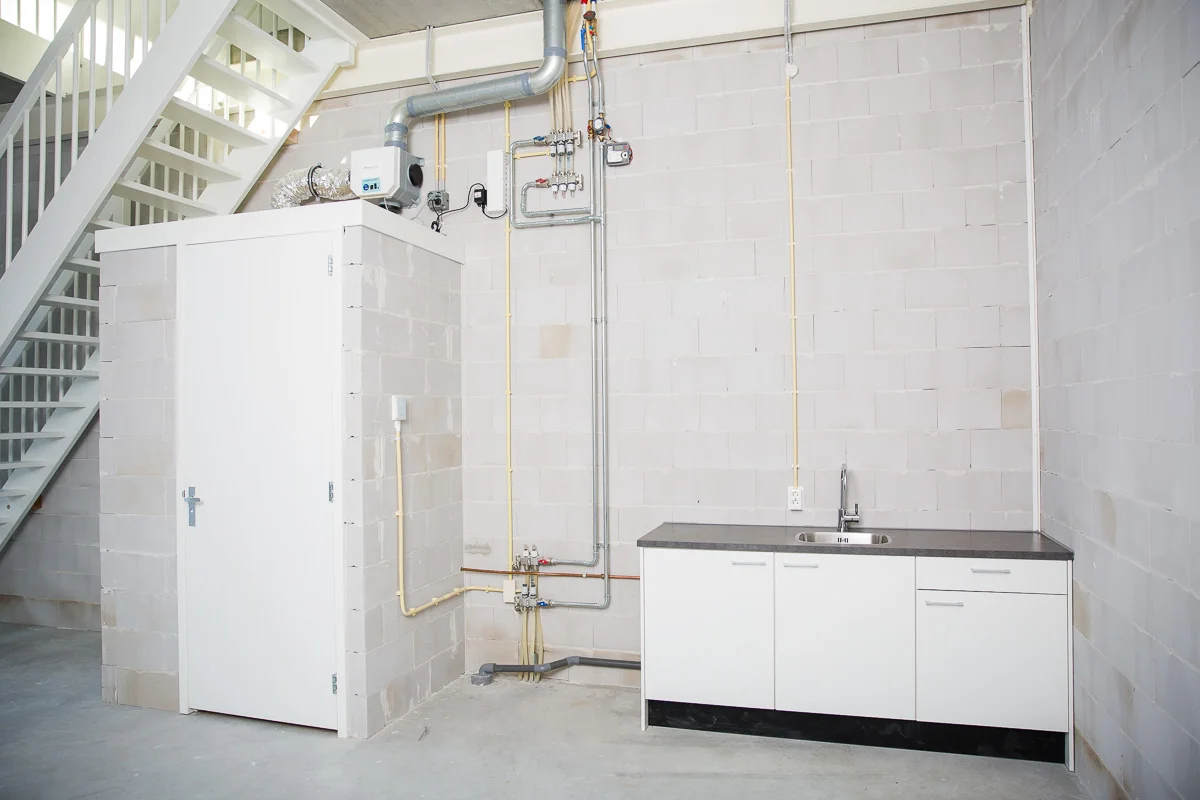 Binnenruimte in een bedrijfsunit aan de Laan van 's-Gravenmade met een eenvoudig keukenblok, technische installaties en een trap naar boven.